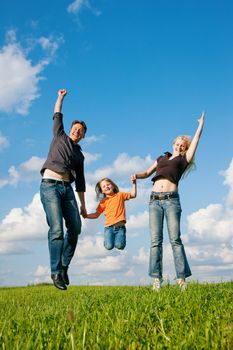 Family - mother, father, child - jumping high in the air on a green meadow at a late summer afternoon