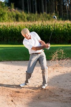 Senior golf player chipping his ball out of a sand trap, ball in motion and lots of sand frozen (short shutter speed)