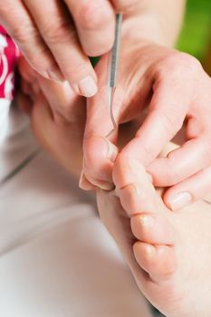 Woman practicing chiropody taking care of a male feet; focus on tool