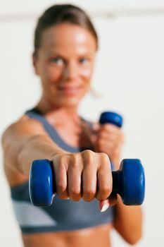 Beautiful woman with a dumbbell exercising in gym (focus is on the dumbbell!)