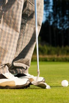 Golf player putting ball into hole, only feet and iron to be seen