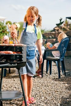 Family having a barbecue party - little kid at the barbecue grill preparing meat and sausages