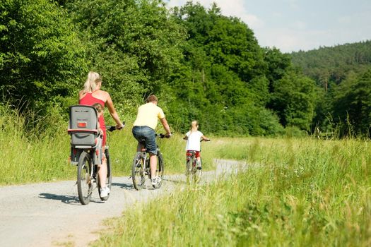 Family with two kids riding their bicycles on a summer day (seen from behind)