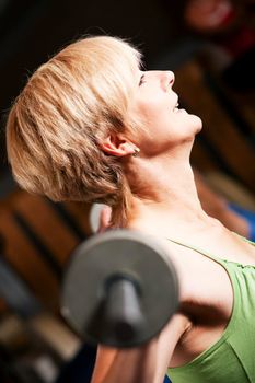 Mature woman in a gym exercising by lifting a barbell