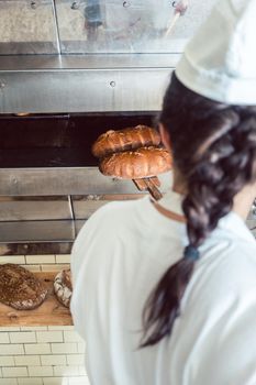 Baker woman getting fresh bread with shovel out of oven