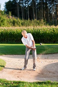 Senior golf player chipping his ball out of a sand trap, ball in motion and lots of sand frozen (short shutter speed)