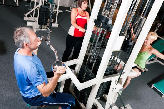 Senior people in a gym exercising on a pulldown machine