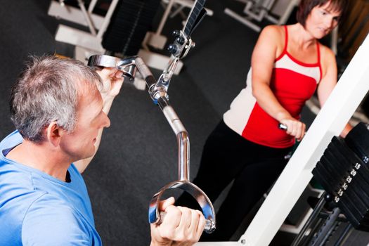 Senior people in a gym exercising on a pulldown machine
