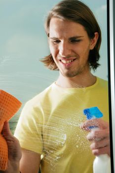 Young man cleaning his windows with spray and sponge