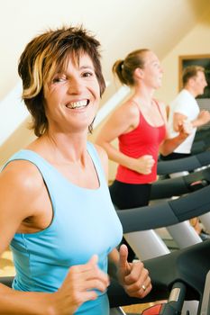 Three happy people running on a treadmill in a gym; slight motion blur on arms of woman in foreground for a dynamic picture