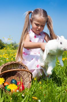 Girl hugging an easter bunny with eggs on a meadow in spring