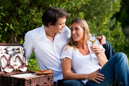 Couple sitting outdoors having a picnic with white wine