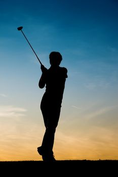 Senior woman playing golf - pictured as a silhouette against an evening sky