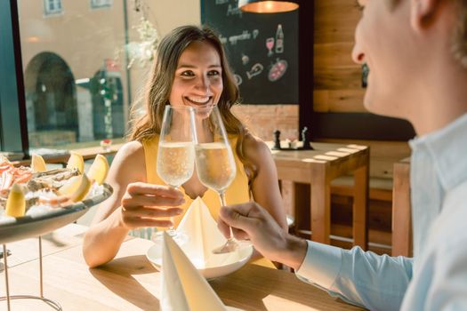 Young and beautiful woman smiling happy while toasting with champagne during a romantic dinner with her partner at a trendy restaurant downtown