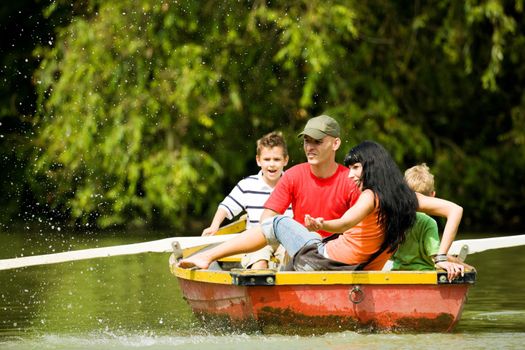 Family with two kids having a boat trip on a lake, in the background lots of trees and flowers