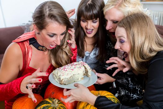 Four young women and best friends wearing Halloween costumes while posing funny before sharing a delicious cake at the party