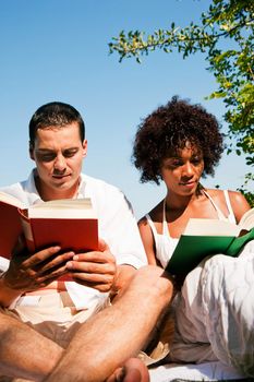 Couple reading books in the sunshine sitting at lake in summerCouple reading books in the sunshine sitting at lake in summer