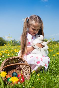 Girl hugging an easter bunny with eggs on a meadow in spring