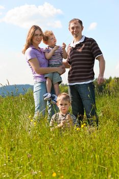 Family with two little boys playing in the grass on a summer meadow carrying one of the kids