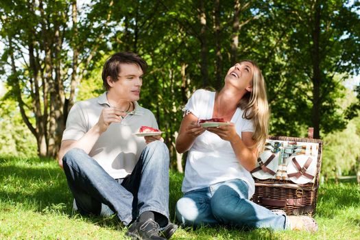 Couple sitting in the grass in summer having a picnic with strawberry cake