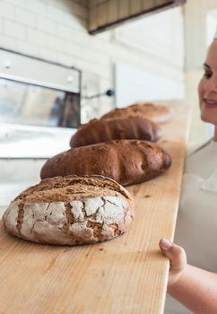 Fresh bread on a board in bakehouse of bakery being held by a female baker