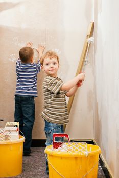 Family concept - two boy painting a wall in their home, one is making hand prints the other one using a paint roll