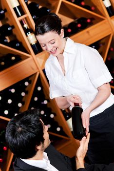 Pretty waitress in a wine bar offers a bottle of red wine to taste it a young mediterranean looking man.