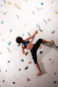 Woman (African-American) exercising at a climbing wall in a gym