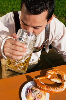 Man in traditional Bavarian costume - Lederhosen - drinking beer and eating pretzel