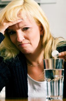 Woman with a really bad migraine dropping a painkiller pill into a glass of water