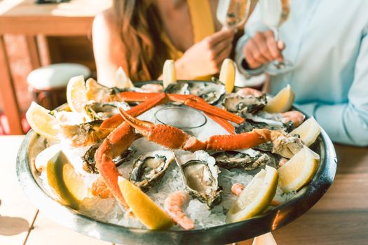 Close-up of fresh oysters and crabs served on ice with slices of lemon at the table of a romantic young couple eating at restaurant
