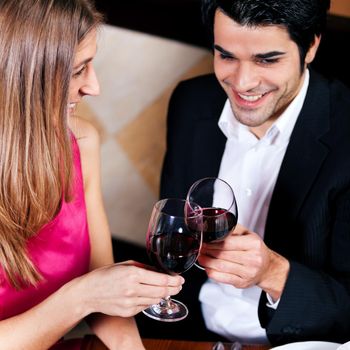 Young couple - man and woman - in a restaurant clinking the red wine glasses; focus on the glasses