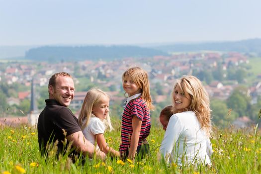 Very happy family with three kids sitting in a meadow with dandelion in the summer sun