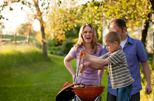 Family having a barbecue party, mother father and son standing around the bbq grill