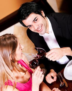 Young couple - man and woman - in a restaurant clinking the red wine glasses; focus on the glasses