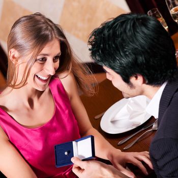 Young man making a wedding proposal offering a ring to his girlfriend in a fancy restaurant
