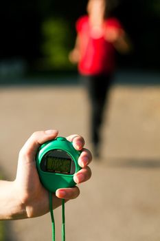 Young woman doing sport outdoors jogging, a trainer is ready to measure her performance