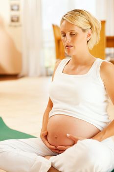 Pregnant woman meditating doing pregnancy yoga sitting on the floor in her home