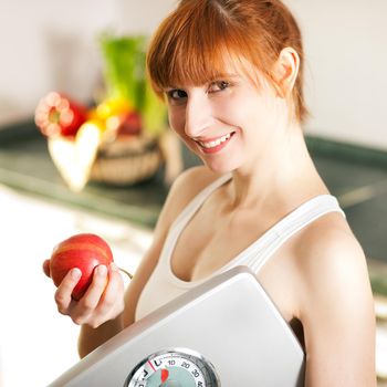 Thin and beautiful woman (only torso) measuring her waist with a tape measure, in the background fruit in a bowl