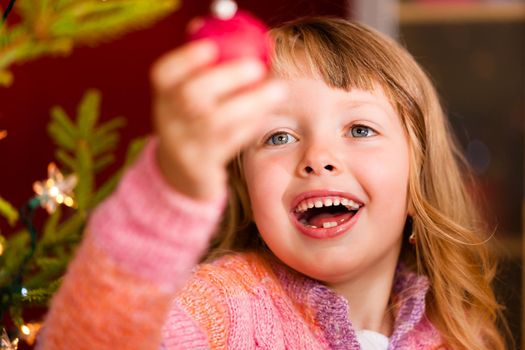 Young girl helping decorating the Christmas tree, holding some Christmas baubles in her hand