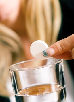 Woman holding a pill over a glass of water (macro)