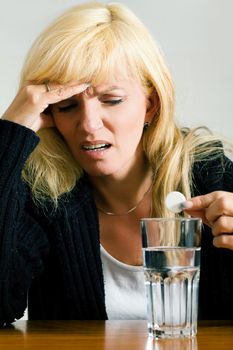 Woman with a really bad migraine dropping a painkiller pill into a glass of water