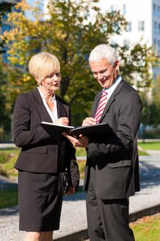 Business people - mature or senior - talking outdoors and discussing a document