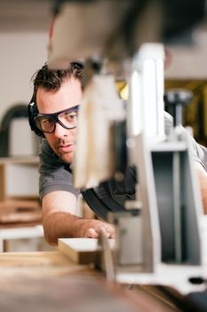 Carpenter working on an electric buzz saw cutting some boards, he is wearing safety glasses and hearing protection to make things safe