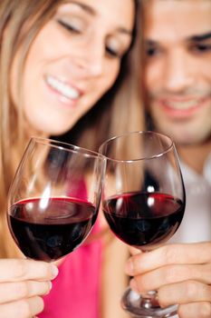 Young couple - man and woman - in a restaurant clinking the red wine glasses; focus on the glasses