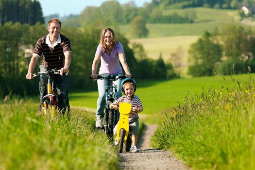 Family with boy child having a weekend excursion on their bikes on a summer day in beautiful landscape