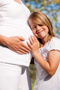 Family affairs - Girl is touching round belly of her pregnant mother in eager anticipation of the new child