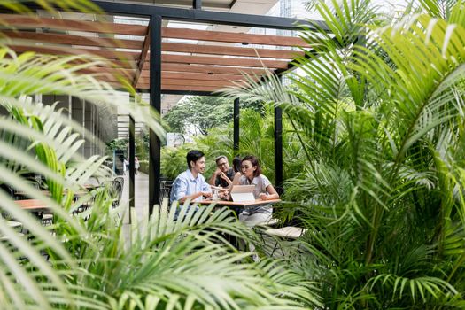 People sitting down at tables outdoors at a modern cafeteria surrounded by green vegetation in Asia