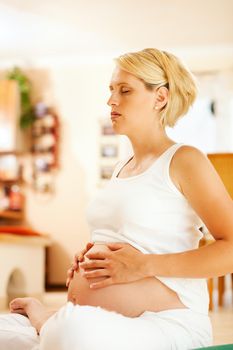 Pregnant woman meditating doing pregnancy yoga sitting on the floor in her home