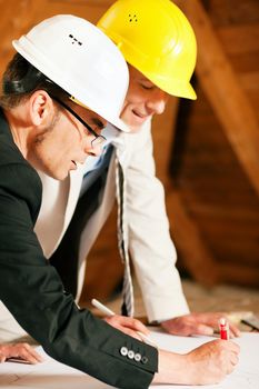 Architect and construction engineer or surveyor discussion plans and blueprints. Both are wearing hardhats and are standing on the construction site of a home indoors